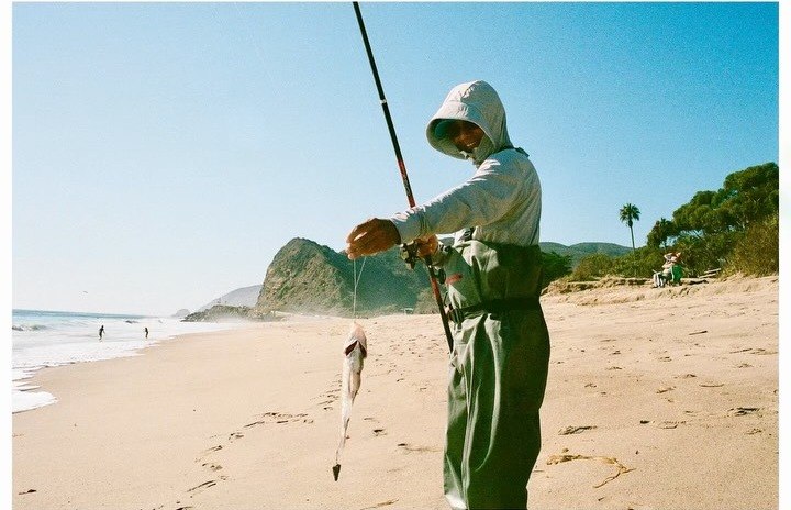 Fisherman in waders holding up a fish he caught on a Malibu beach
