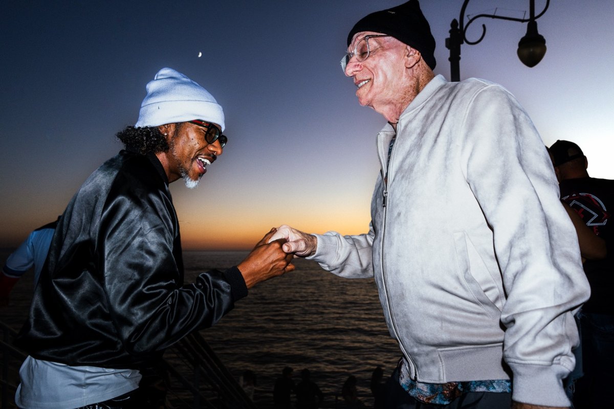 Two strangers fist-bumping and laughing on Santa Monica Pier at sunset