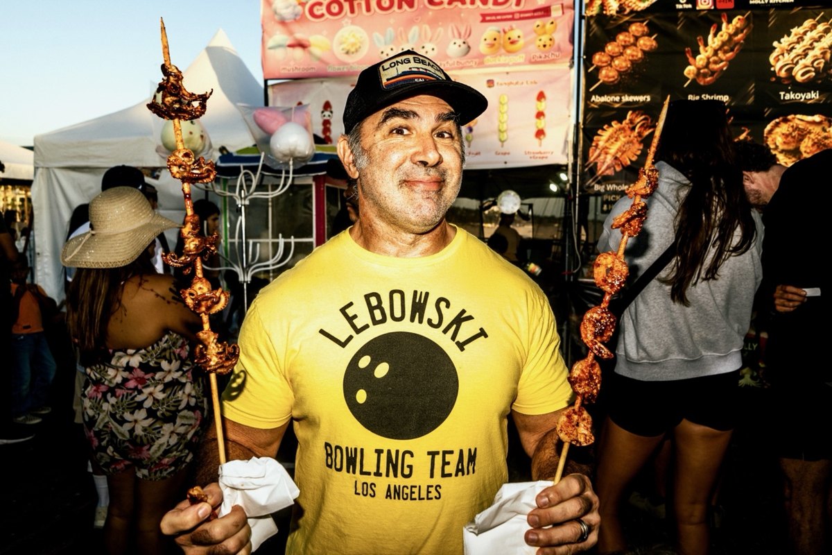 Man in a yellow Lebowski bowling shirt holding skewers of food on the Santa Monica boardwalk