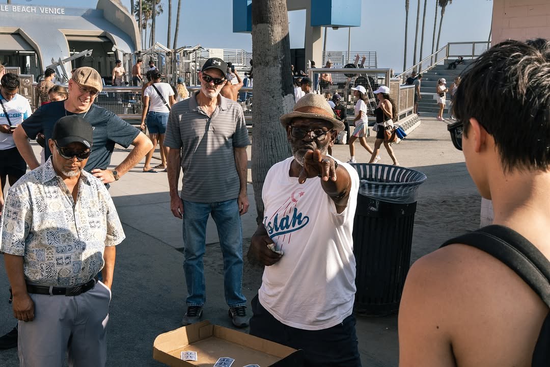 Laughing man in a beige sweater pointing at the camera on the Venice Beach boardwalk